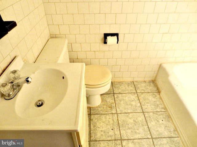 bathroom with sink, a bath, tile patterned floors, toilet, and tile walls