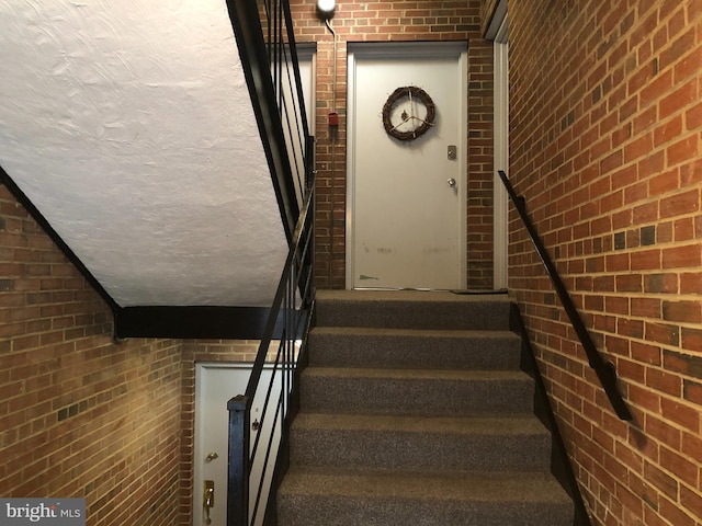 stairs with carpet floors, brick wall, and a textured ceiling