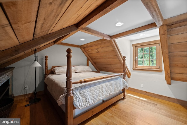 bedroom with vaulted ceiling with beams, a stone fireplace, wooden ceiling, and light wood-type flooring