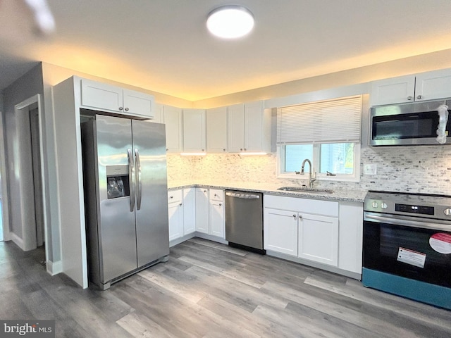 kitchen with light stone countertops, white cabinetry, sink, stainless steel appliances, and light hardwood / wood-style flooring