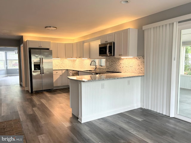 kitchen featuring dark wood-type flooring, sink, appliances with stainless steel finishes, light stone counters, and kitchen peninsula