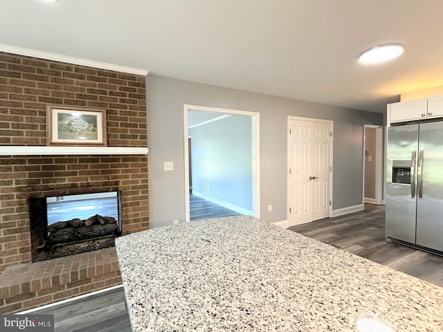 interior space featuring a brick fireplace, stainless steel fridge with ice dispenser, dark hardwood / wood-style floors, light stone counters, and white cabinetry