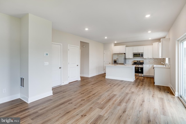 kitchen with white cabinetry, tasteful backsplash, light hardwood / wood-style flooring, appliances with stainless steel finishes, and a kitchen island