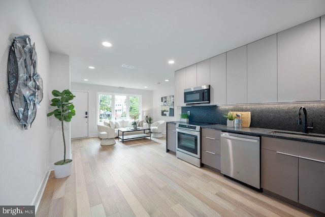 kitchen featuring appliances with stainless steel finishes, light hardwood / wood-style flooring, backsplash, and sink