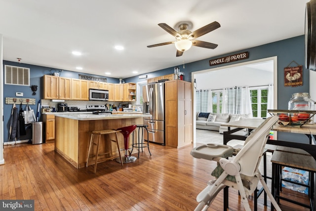 kitchen featuring a center island, light hardwood / wood-style flooring, appliances with stainless steel finishes, tasteful backsplash, and a breakfast bar area