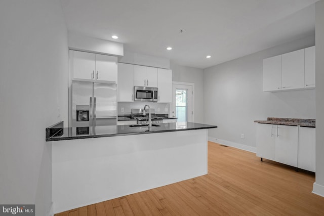 kitchen with kitchen peninsula, white cabinetry, stainless steel appliances, and light hardwood / wood-style floors