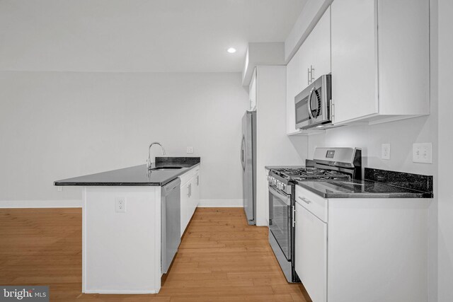 kitchen with kitchen peninsula, light wood-type flooring, stainless steel appliances, sink, and white cabinetry