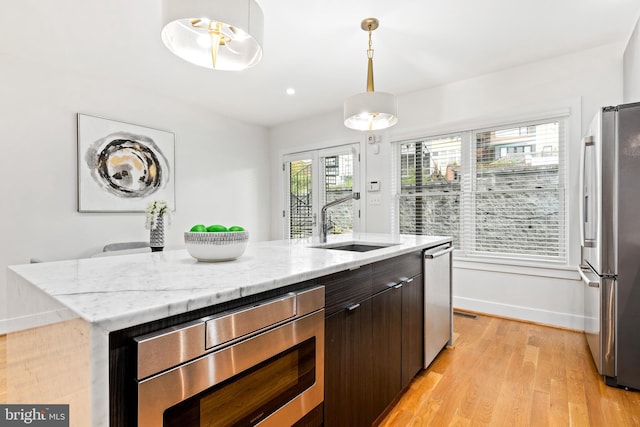 kitchen featuring sink, wall chimney range hood, light hardwood / wood-style flooring, pendant lighting, and a kitchen bar