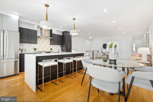 kitchen with sink, wall chimney exhaust hood, stainless steel appliances, light hardwood / wood-style flooring, and decorative light fixtures