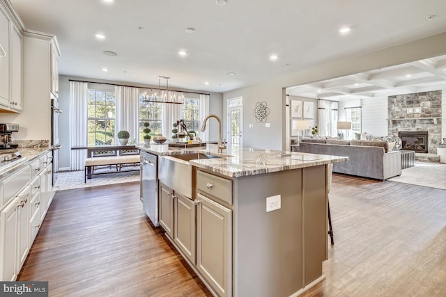 kitchen with sink, wood-type flooring, a center island with sink, a fireplace, and white cabinetry