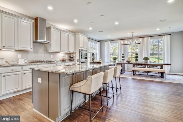 kitchen with wall chimney exhaust hood, hanging light fixtures, dark hardwood / wood-style flooring, a kitchen island with sink, and appliances with stainless steel finishes