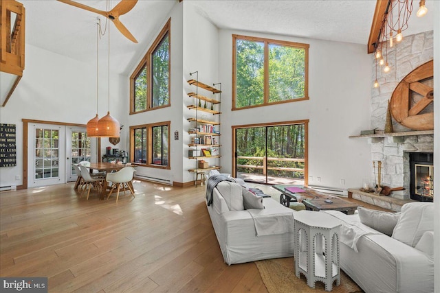 living room featuring a stone fireplace, high vaulted ceiling, light hardwood / wood-style floors, and a textured ceiling