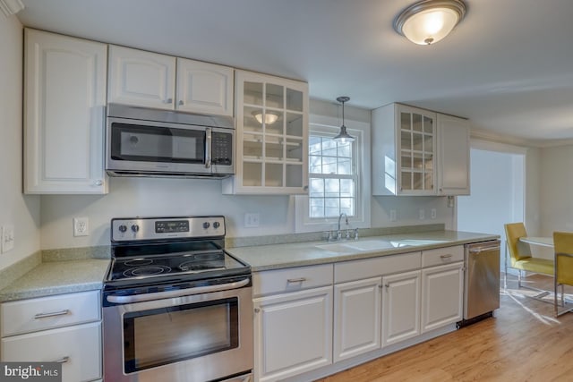 kitchen featuring sink, hanging light fixtures, light hardwood / wood-style flooring, white cabinets, and appliances with stainless steel finishes