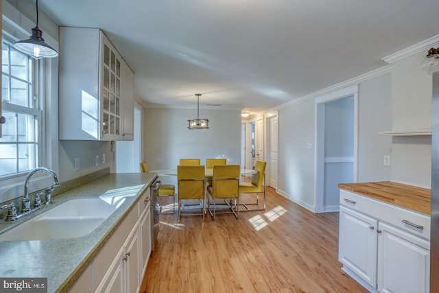 kitchen featuring white cabinets, sink, hanging light fixtures, light wood-type flooring, and ornamental molding