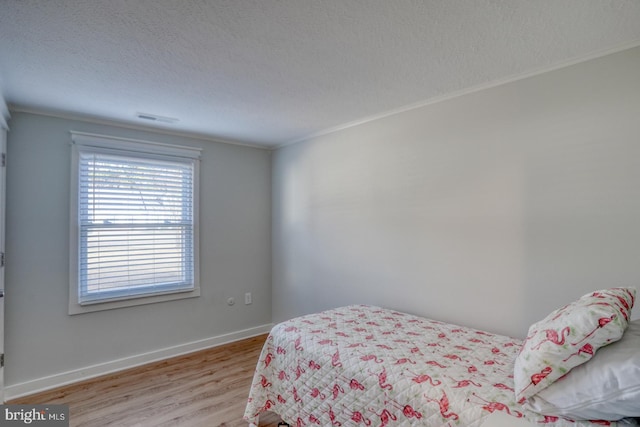 bedroom featuring a textured ceiling, light hardwood / wood-style floors, and crown molding