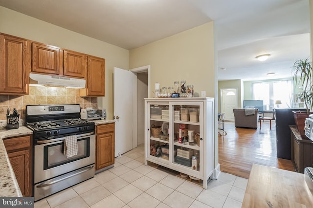 kitchen with light stone countertops, gas range, light hardwood / wood-style flooring, and backsplash