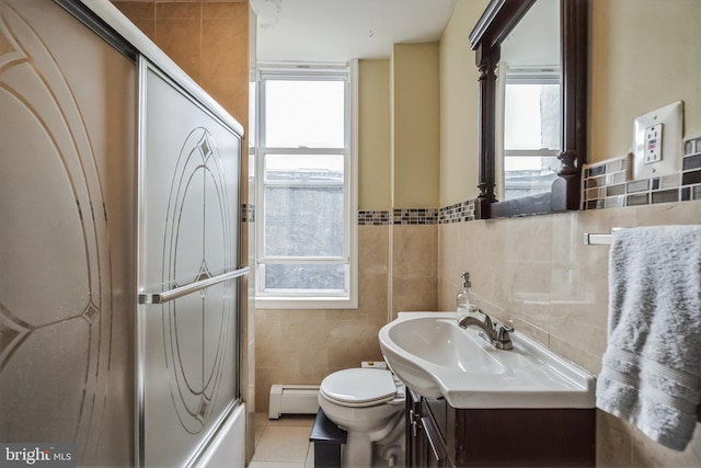 full bathroom featuring tile walls, vanity, combined bath / shower with glass door, toilet, and a baseboard heating unit