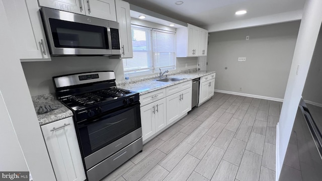 kitchen with light stone countertops, sink, white cabinets, and appliances with stainless steel finishes