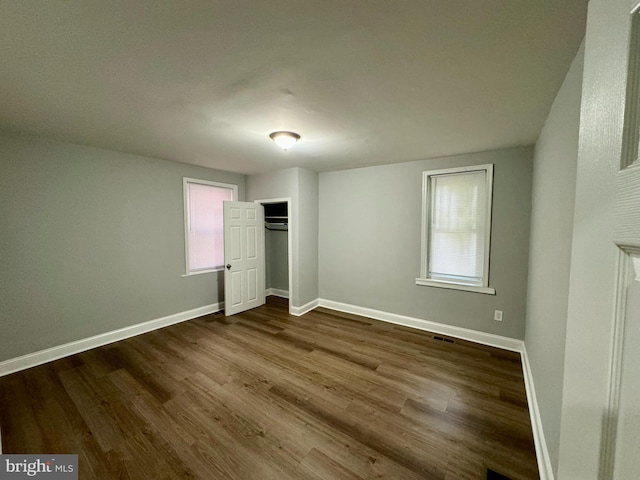 unfurnished bedroom featuring multiple windows, a closet, and hardwood / wood-style flooring