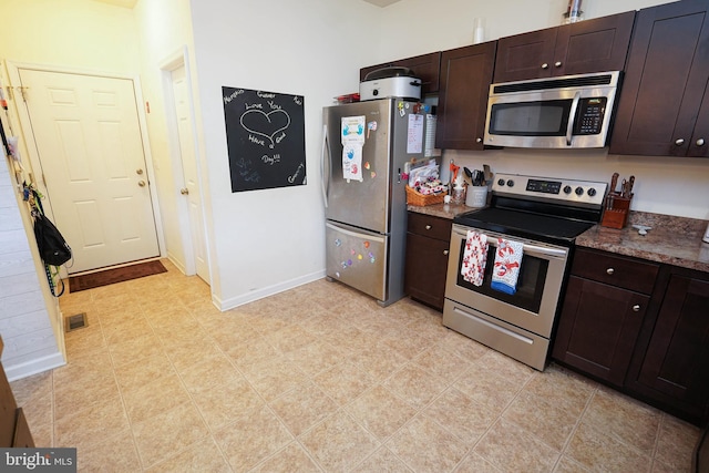 kitchen with dark brown cabinets, dark stone counters, and appliances with stainless steel finishes