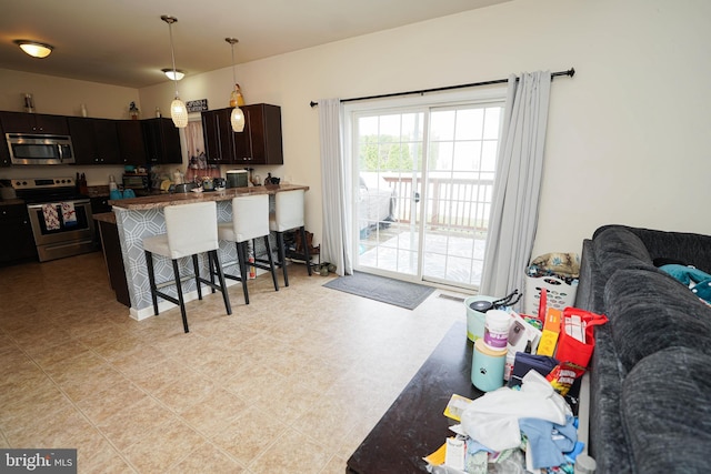 kitchen featuring a kitchen bar, hanging light fixtures, kitchen peninsula, stainless steel appliances, and dark brown cabinets