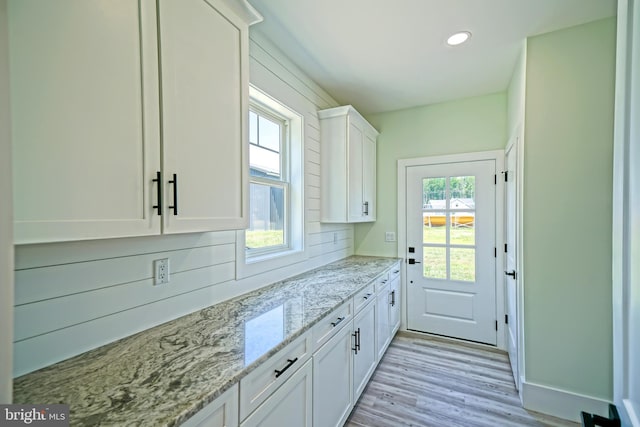 kitchen with white cabinetry, light stone countertops, and light wood-type flooring