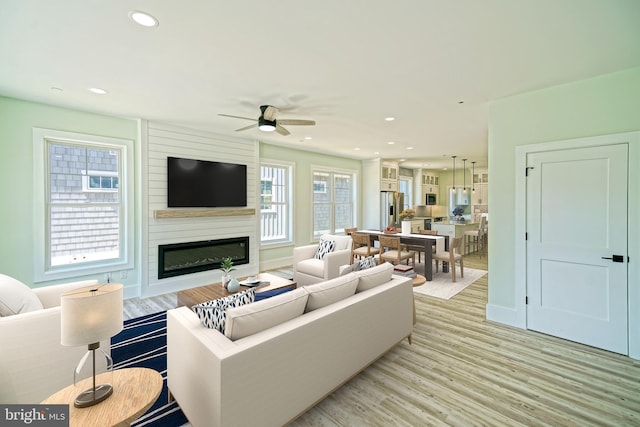 living room featuring a large fireplace, light hardwood / wood-style floors, and ceiling fan