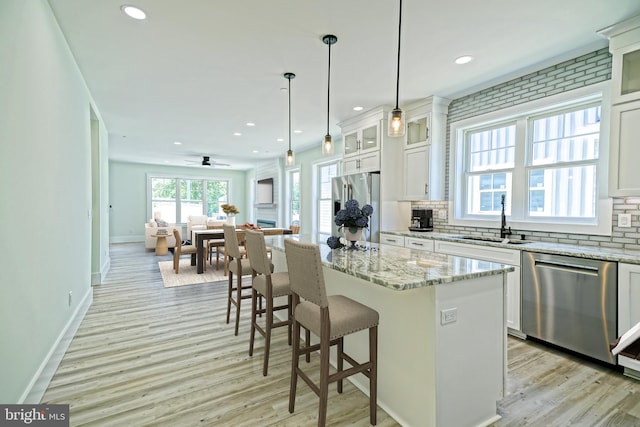 kitchen with sink, a kitchen island, light stone counters, white cabinetry, and stainless steel appliances