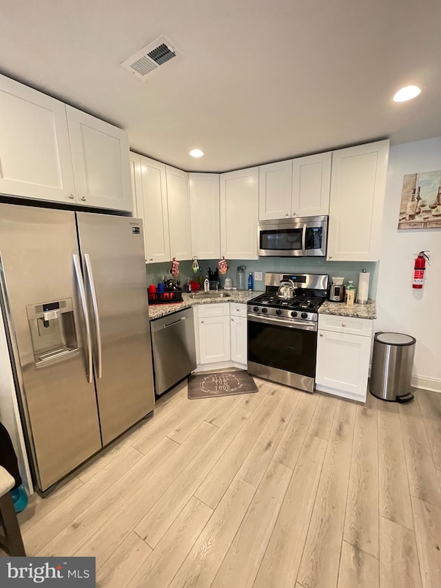 kitchen with white cabinetry, sink, stainless steel appliances, light stone counters, and light wood-type flooring