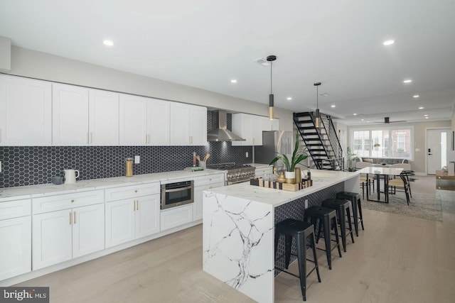 kitchen with a kitchen island, stainless steel appliances, wall chimney range hood, and light wood-type flooring