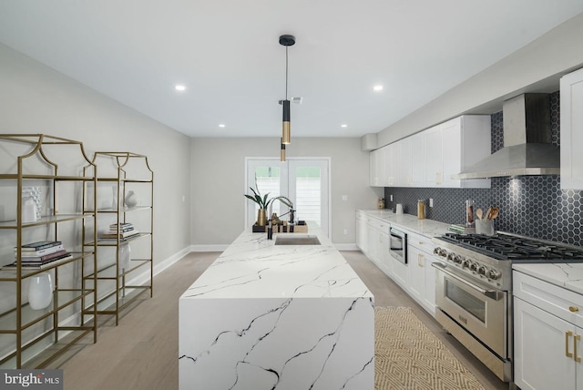 kitchen with wall chimney exhaust hood, sink, stainless steel stove, white cabinetry, and an island with sink