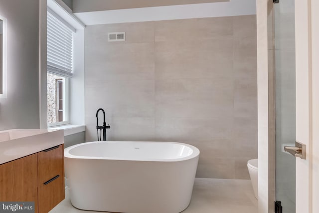 bathroom featuring vanity, toilet, tile walls, and a bathing tub