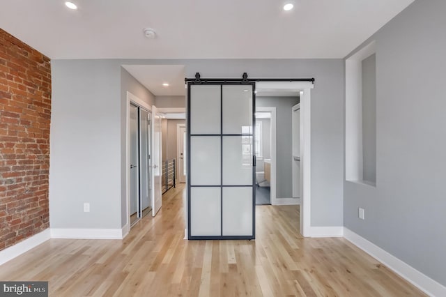 unfurnished room with a barn door, light hardwood / wood-style flooring, and brick wall