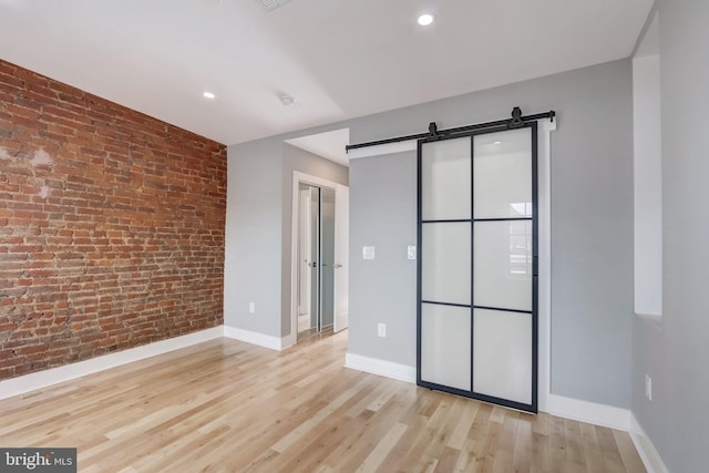 unfurnished bedroom with a barn door, brick wall, and light wood-type flooring