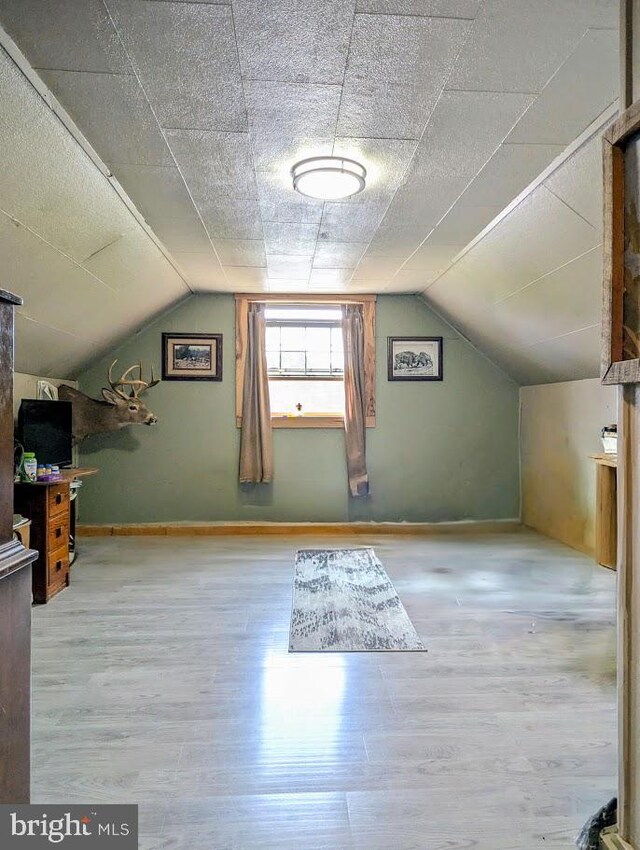 bonus room with a textured ceiling, light wood-type flooring, and lofted ceiling