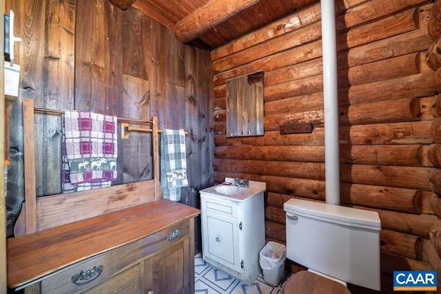 bathroom featuring beam ceiling, rustic walls, wooden ceiling, and toilet