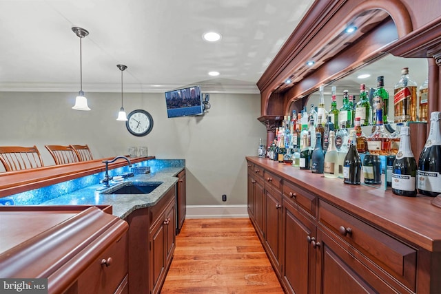 bar with light wood-type flooring, crown molding, sink, decorative light fixtures, and stone countertops