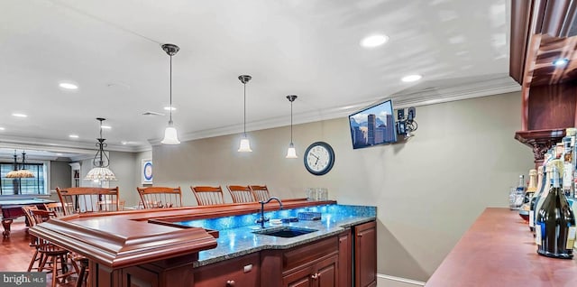 bar featuring light stone counters, ornamental molding, sink, and hanging light fixtures