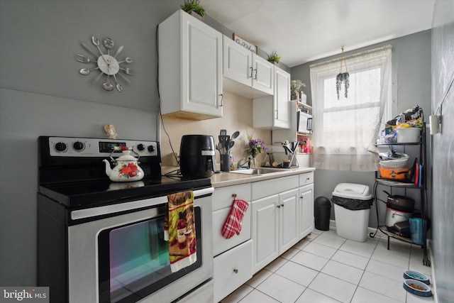 kitchen with white cabinetry, light tile patterned flooring, stainless steel electric range oven, and sink