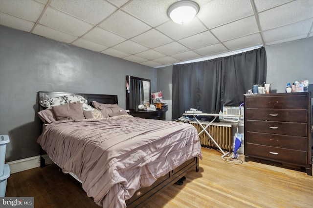 bedroom with a drop ceiling and light wood-type flooring