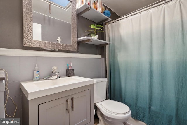 bathroom featuring walk in shower, vanity, toilet, and tile walls