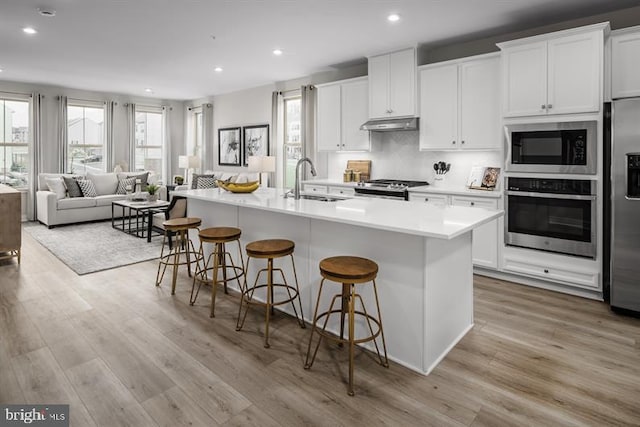 kitchen with appliances with stainless steel finishes, a breakfast bar area, white cabinets, and an island with sink