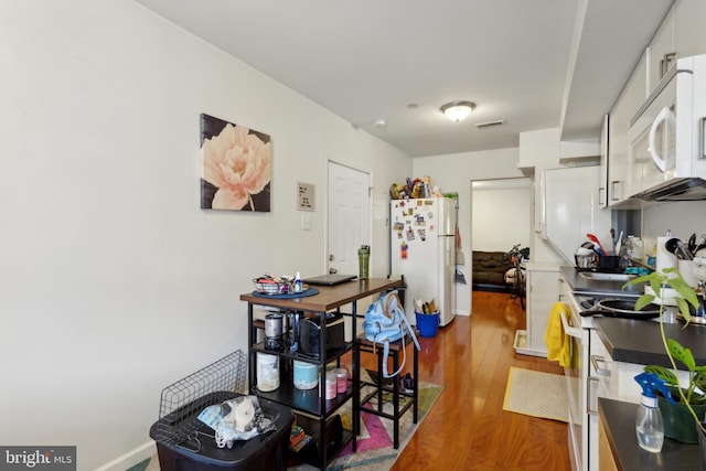 kitchen with white cabinets, wood-type flooring, and white appliances