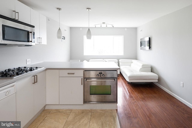 kitchen with hardwood / wood-style floors, white cabinets, appliances with stainless steel finishes, decorative light fixtures, and kitchen peninsula