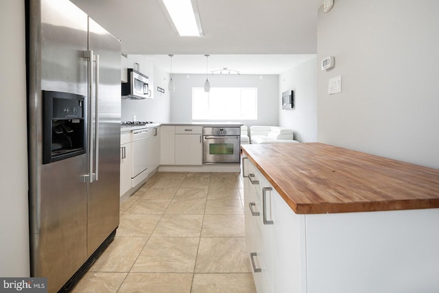 kitchen featuring appliances with stainless steel finishes, butcher block countertops, white cabinetry, and hanging light fixtures