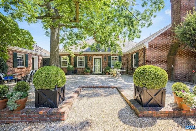 view of front of house featuring a patio, brick siding, and a shingled roof