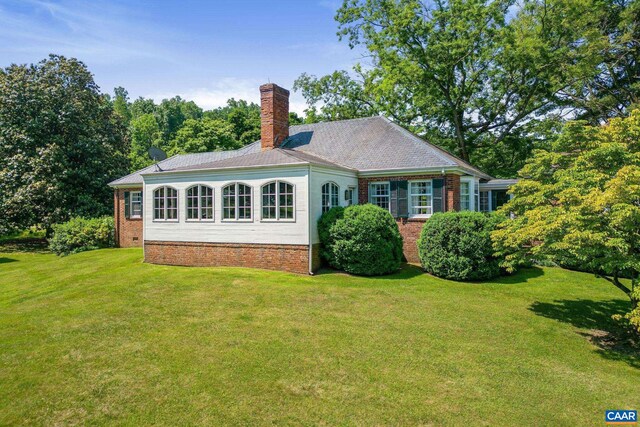 rear view of property with a yard, brick siding, and a chimney