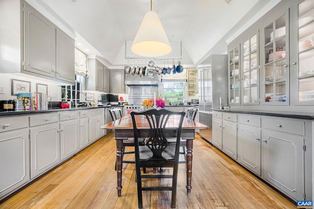 kitchen with dark countertops, gray cabinets, lofted ceiling, light wood-style floors, and glass insert cabinets