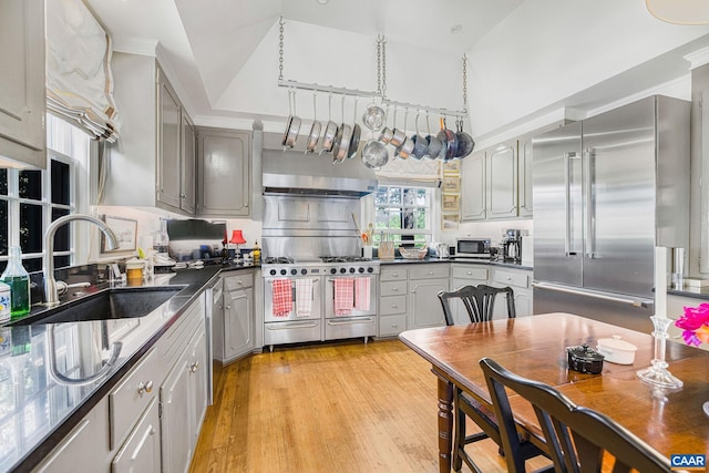 kitchen featuring premium appliances, gray cabinets, dark countertops, and a sink