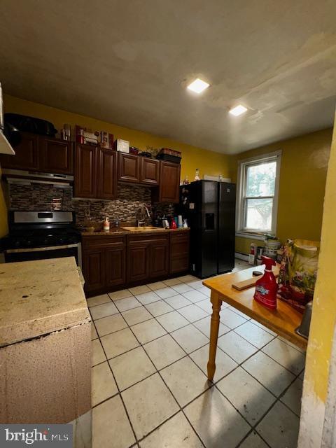 kitchen featuring electric range, black fridge with ice dispenser, light tile patterned floors, and sink